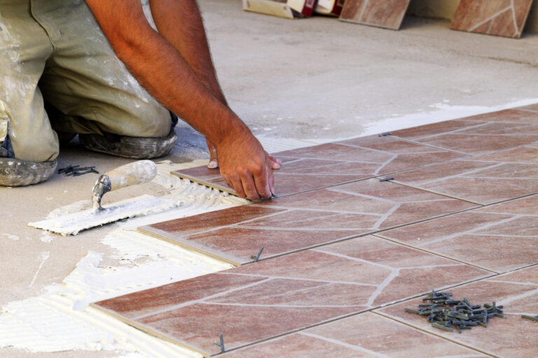 A person installing tiles on a floor using a trowel and spacers.